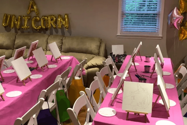Unicorn themed paint party setup with easels and pink table decor